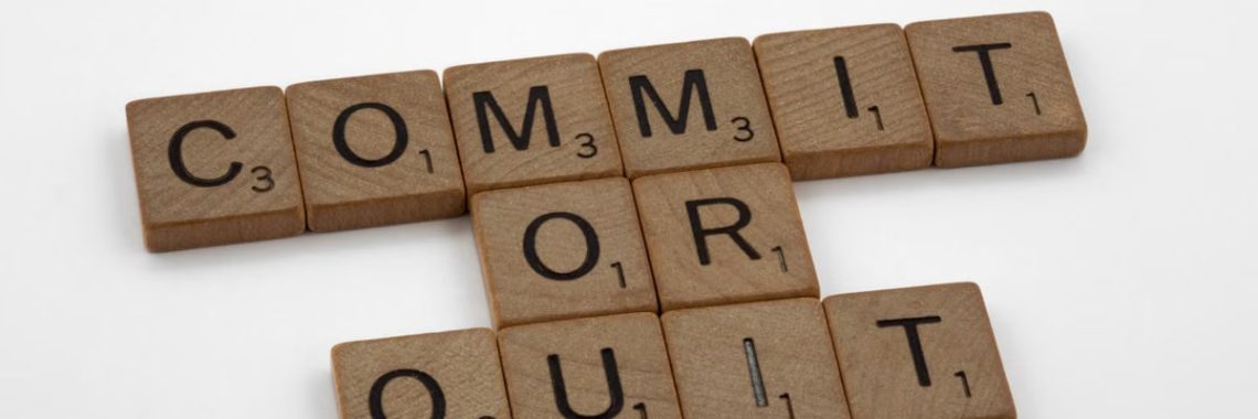 Wooden Scrabble tiles arranged to form the words 'Commit or Quit' on a white background.